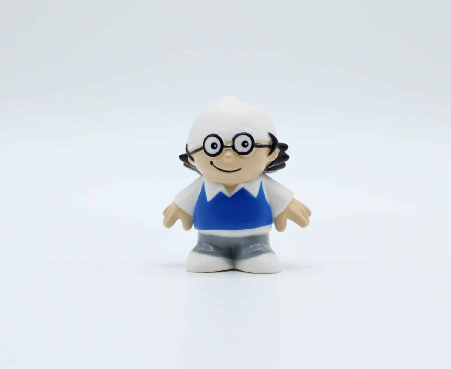 Kleine Figur mit Brille, blauem Oberteil, grauer Hose, weißen Schuhen, schwarzen Haaren.